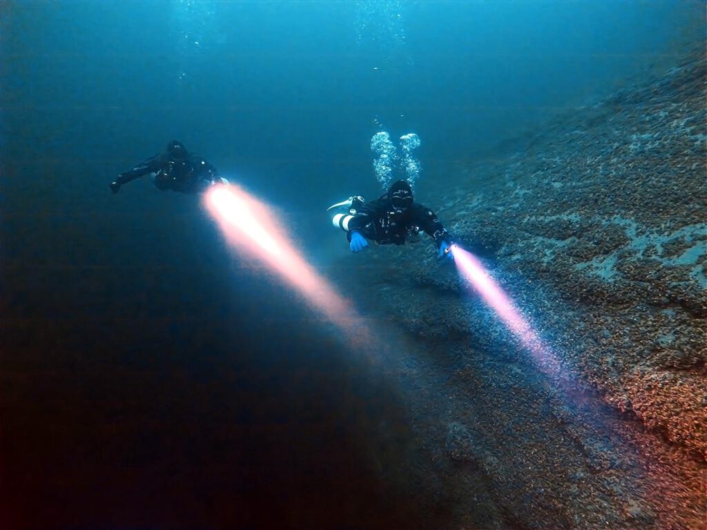 Zwei Taucher im Freiwasser mit starken Lampen.